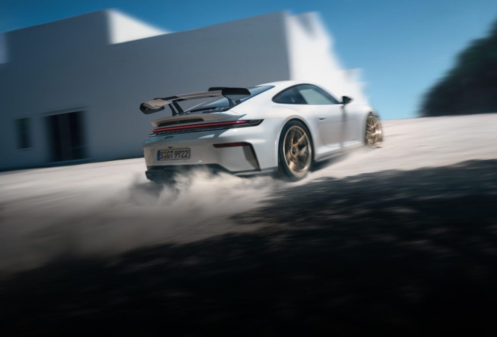 Rear three-quarter action shot of a white Porsche 911 accelerating with dust behind it, symbolizing Porsche’s next 911 and pure driving pleasure.