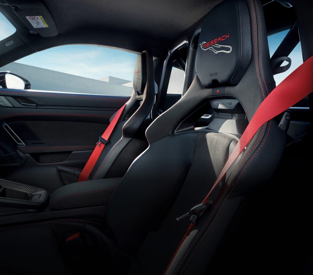 Interior of a Porsche 911 showing black bucket seats with red seat belts and sporty detailing, reflecting Porsche’s next 911 and pure driving pleasure.