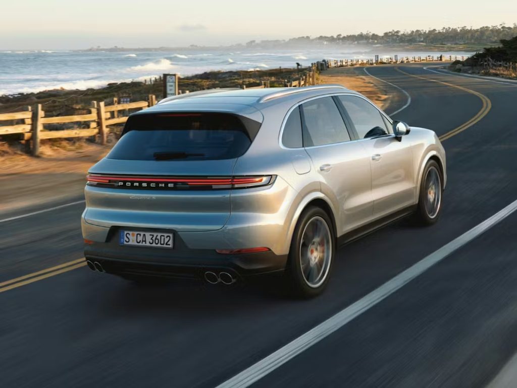 Silver Porsche Cayenne driving along a coastal road, highlighting the performance engineering that helps define the luxury performance SUV segment.