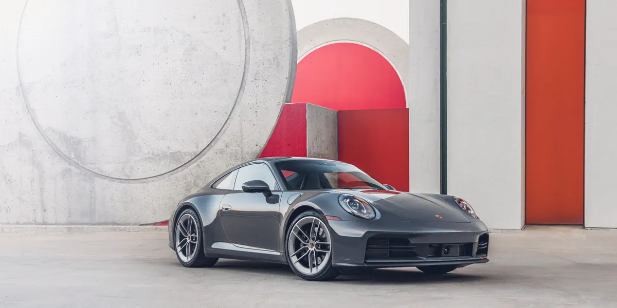 2026 Porsche 911 Carrera side view against modern concrete and red architecture