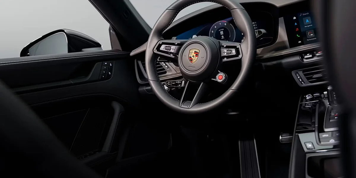 Interior view of 2026 Porsche 911 Carrera 4S Cabriolet showing driver-focused cockpit with digital display, leather-trimmed steering wheel, and premium comfort controls.