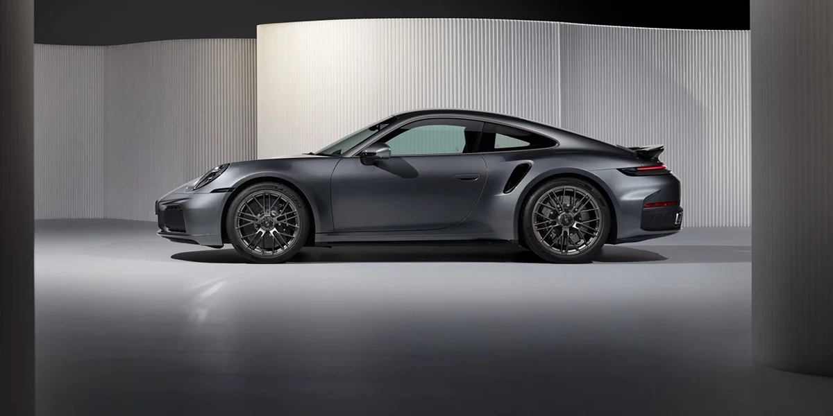 Side profile of the 2026 Porsche 911 Turbo in matte gray, showcasing wide stance and sporty wheels.