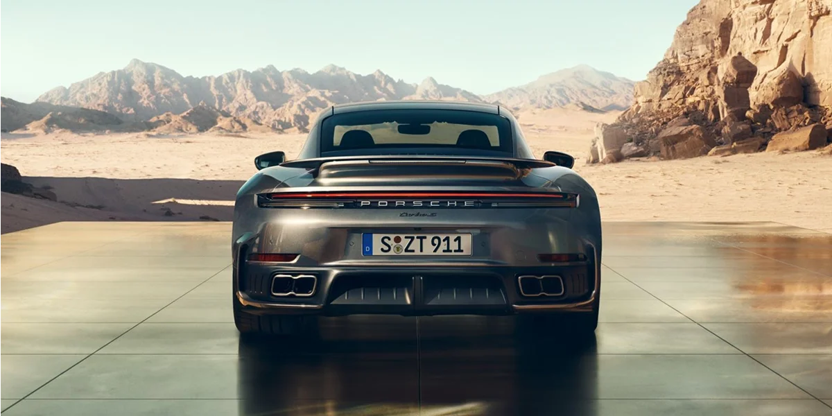 Rear view of the 2026 Porsche 911 Turbo S in metallic gray, parked against desert mountains backdrop.