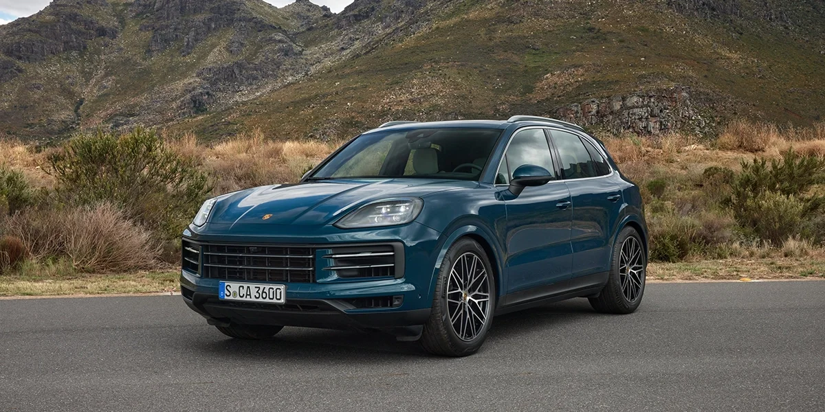 2026 Porsche Cayenne parked on asphalt with rugged mountains in the background.