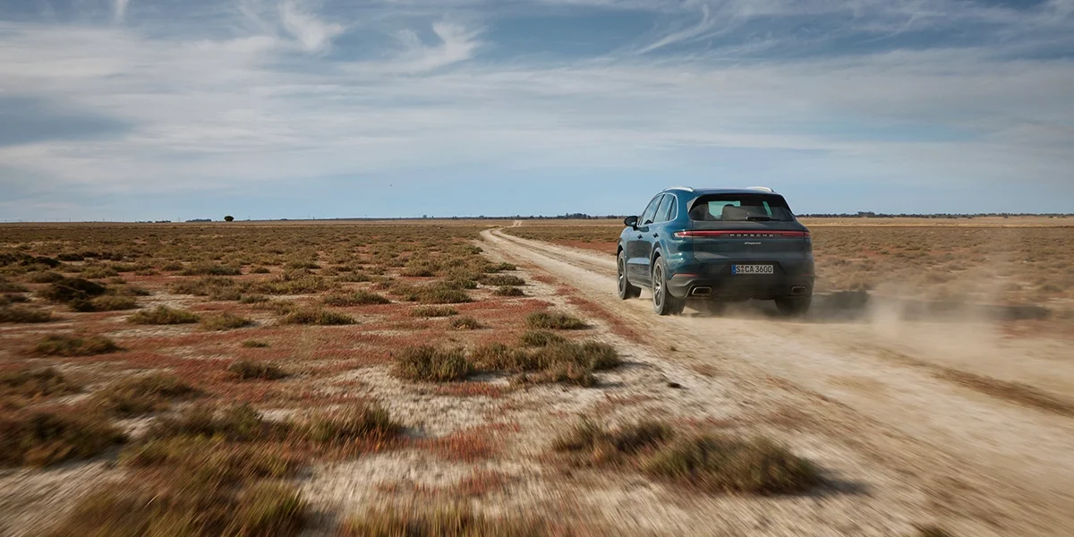 2026 Porsche Cayenne driving on a dirt road in a wide open desert landscape.