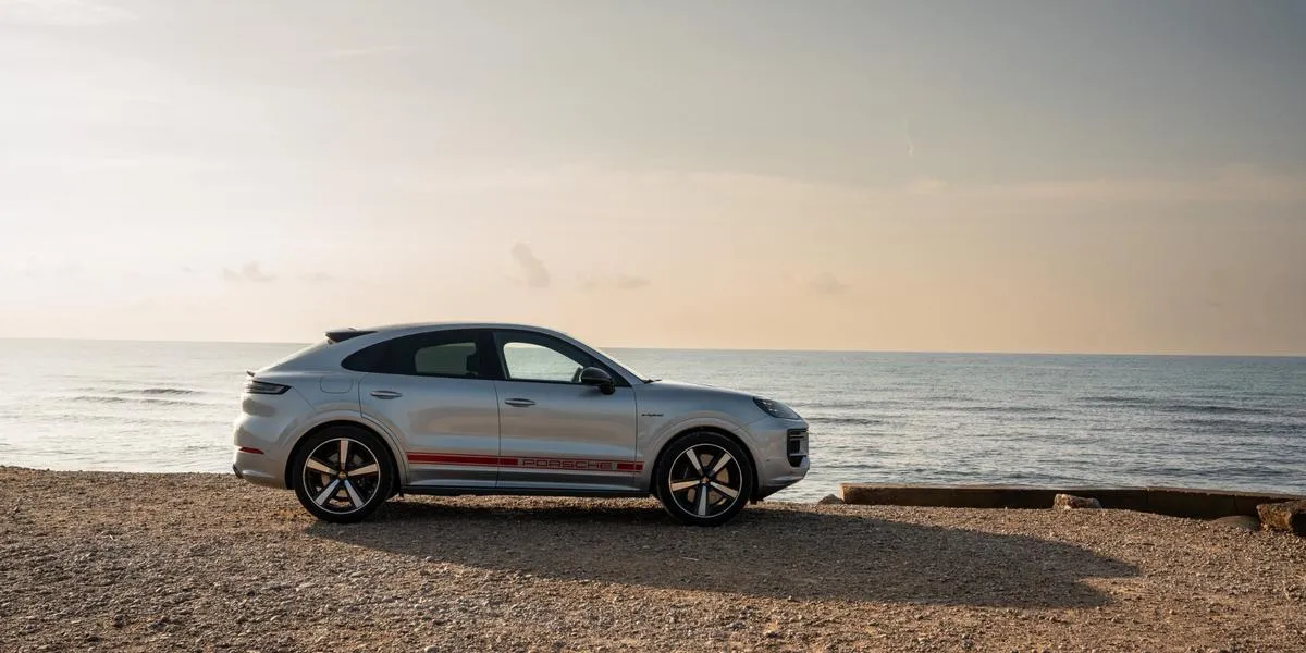 Side profile of the 2026 Porsche Cayenne with red Porsche livery parked by the sea