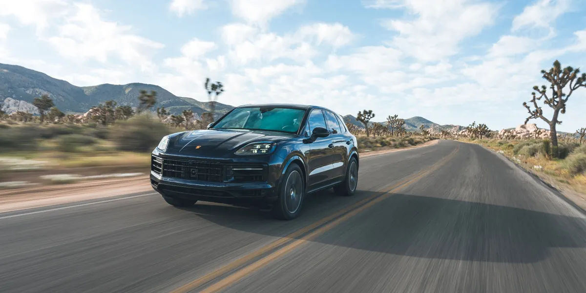 Front view of a Porsche Cayenne E-Hybrid driving through a scenic desert road.