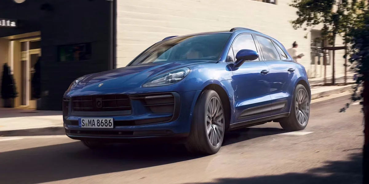 Blue Porsche Macan GTS luxury SUV driving through the city, showcasing aggressive front fascia and sporty design.