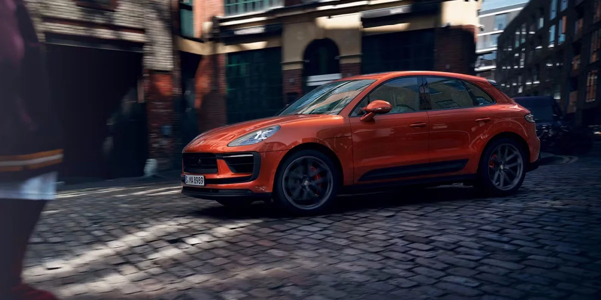 Orange Porsche Macan GTS luxury SUV navigating cobblestone streets with track-inspired handling dynamics.