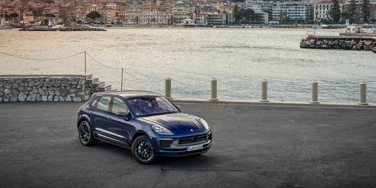 Front view of blue Porsche Macan T with mountains at sunrise in the background