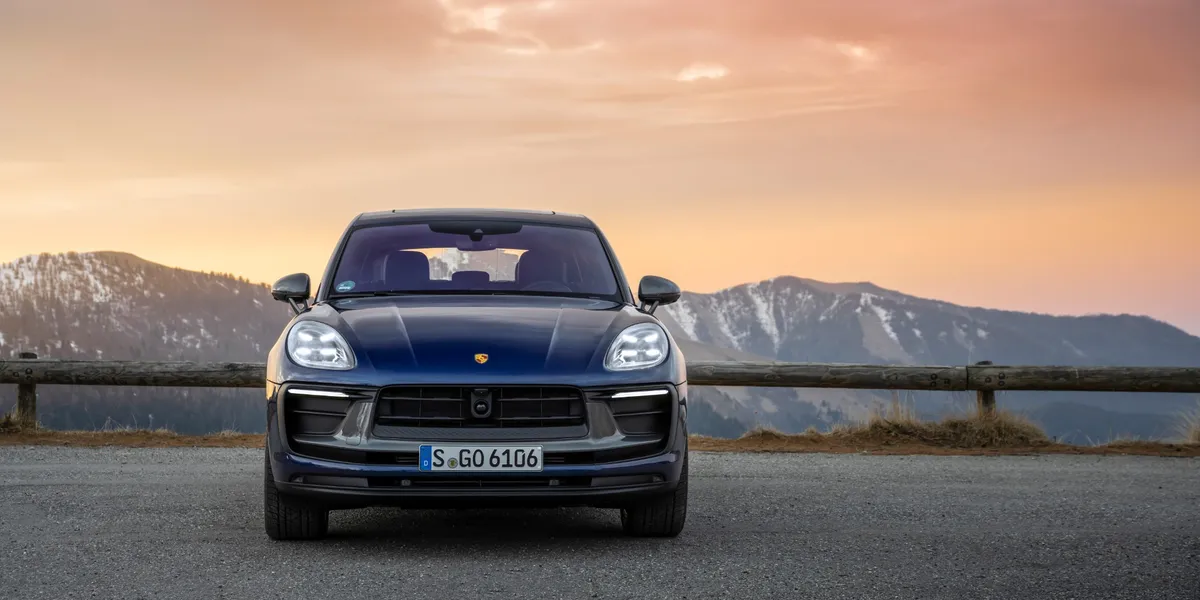 Blue Porsche Macan T parked near harbor with a Mediterranean town in the background