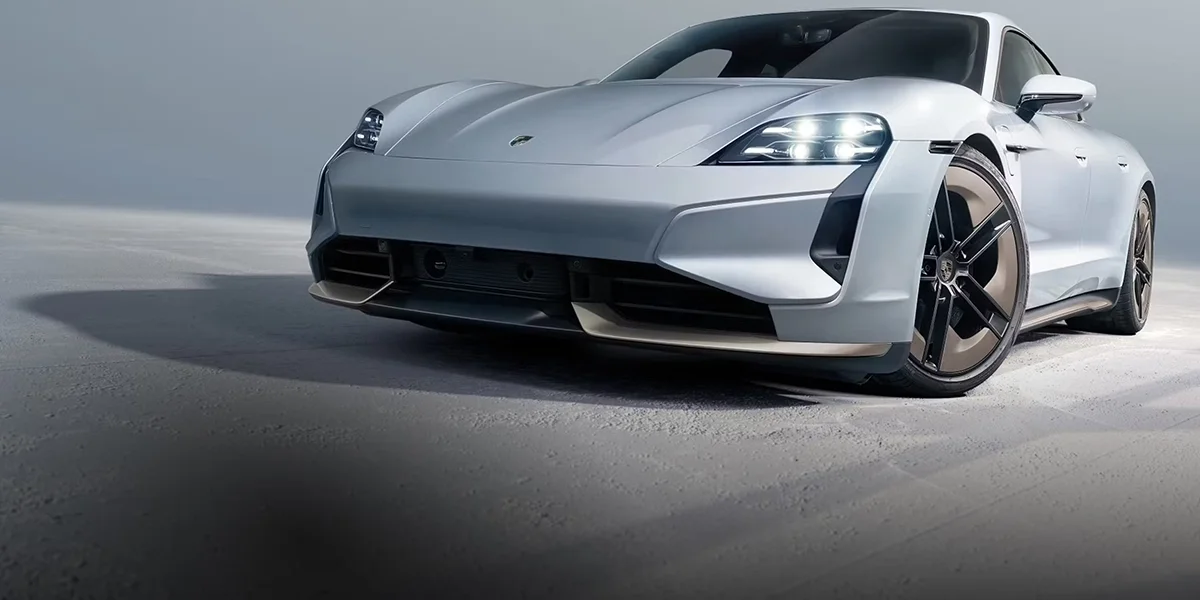 Porsche Taycan in metallic silver parked against a modern architectural building with bold geometric design.