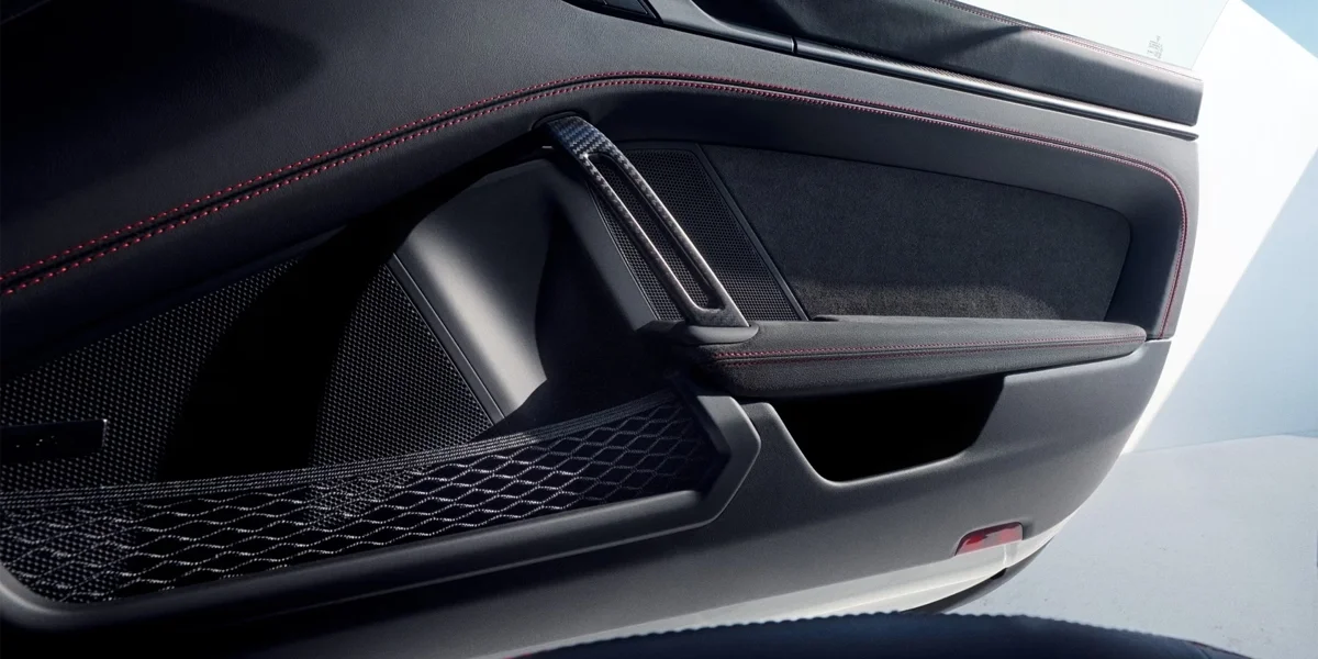 Porsche 911 GT3 interior door panel with carbon-fiber trim, fabric pull strap, and red stitching.