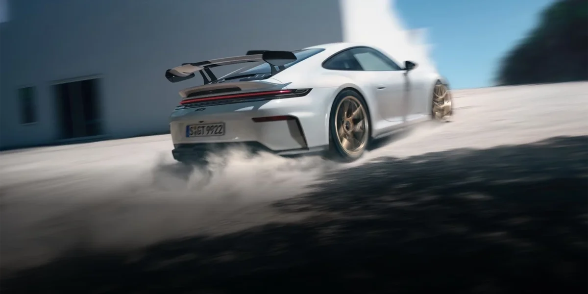 Porsche 911 GT3 cornering at speed, rear three-quarter view with wing visible and dust trailing.