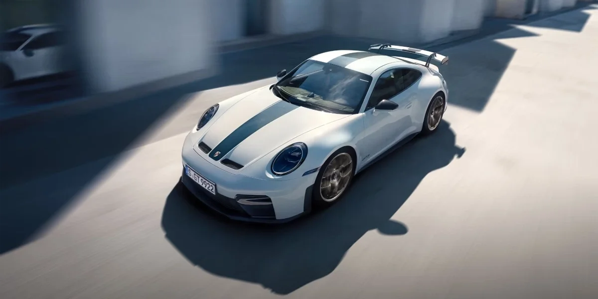 Porsche 911 GT3 driving on a sunlit road, front three-quarter angle with rear wing visible.