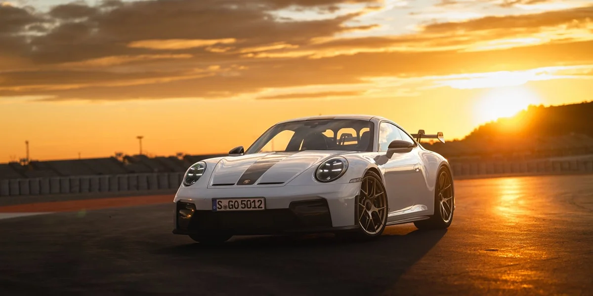 Rear view of Porsche 911 GT3 at sunrise, taillights illuminated, wing silhouette visible.