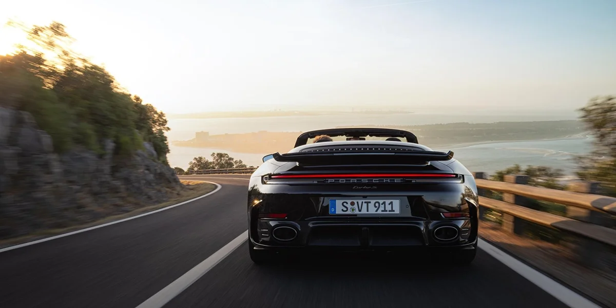 Side profile of a Porsche 911 Turbo S Cabriolet in a studio with a white backdrop, red convertible top folded.