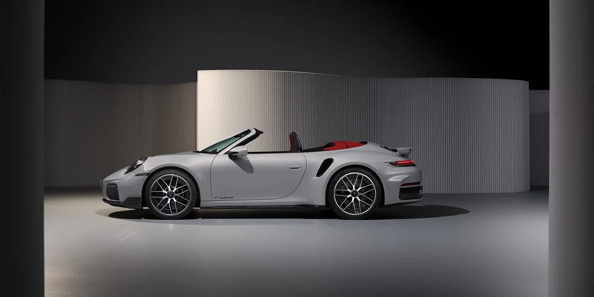 Porsche 911 Turbo S Cabriolet driving on a mountain road at sunset, front three-quarter view.