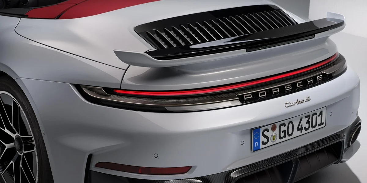 Rear view of Porsche 911 Turbo S Cabriolet driving on a curving mountain road at sunset.