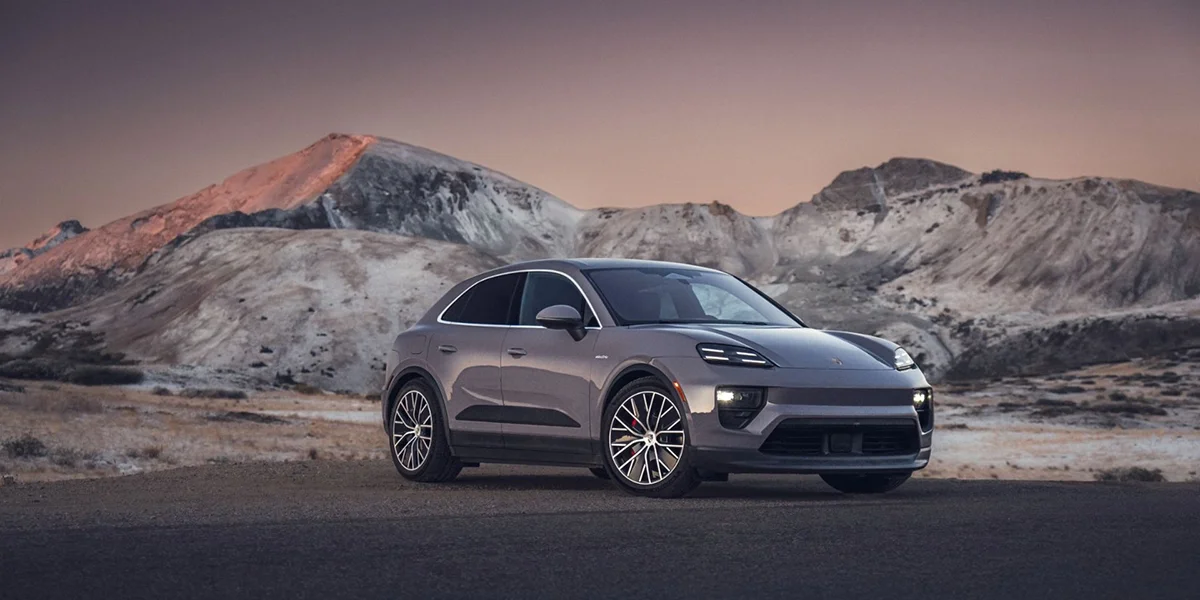 Front three-quarter view of the 2024 Porsche Macan 4S in metallic gray, parked against scenic mountain backdrop at sunset.