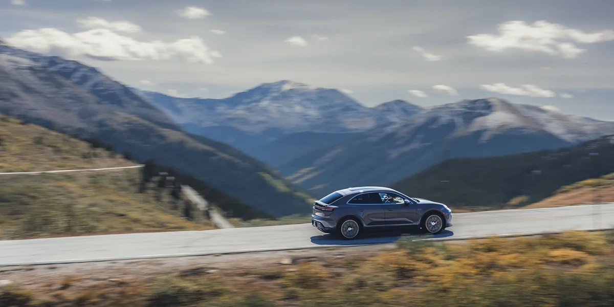 Side view of Porsche Macan 4S in motion against expansive mountain backdrop, emphasizing sporty silhouette.