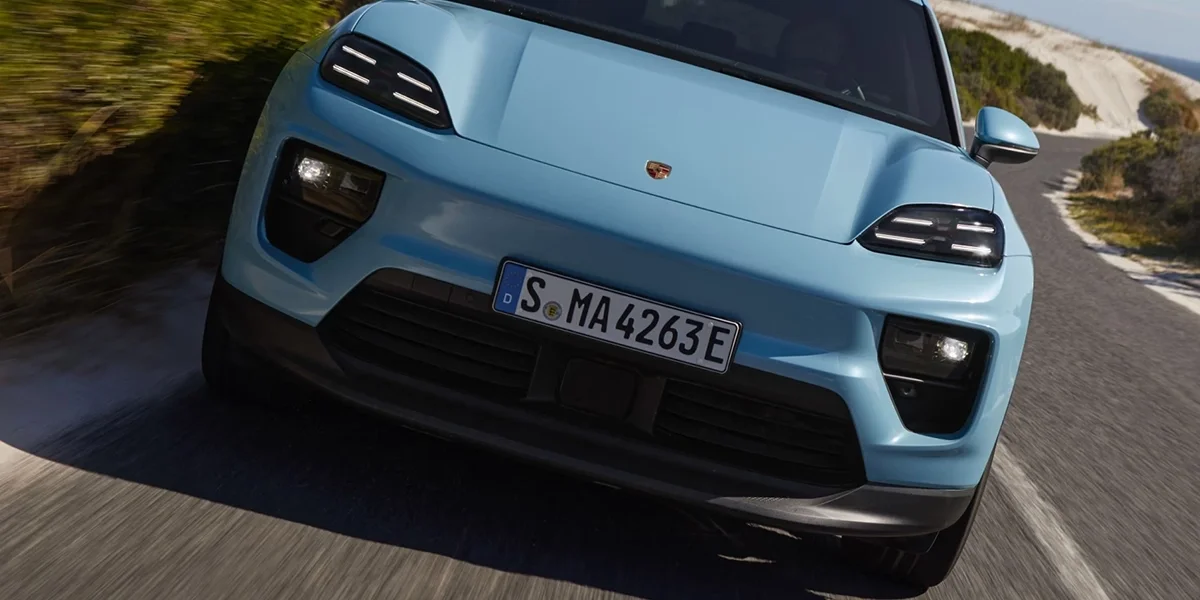 Front view of the Porsche Macan Electric driving on a coastal road.
