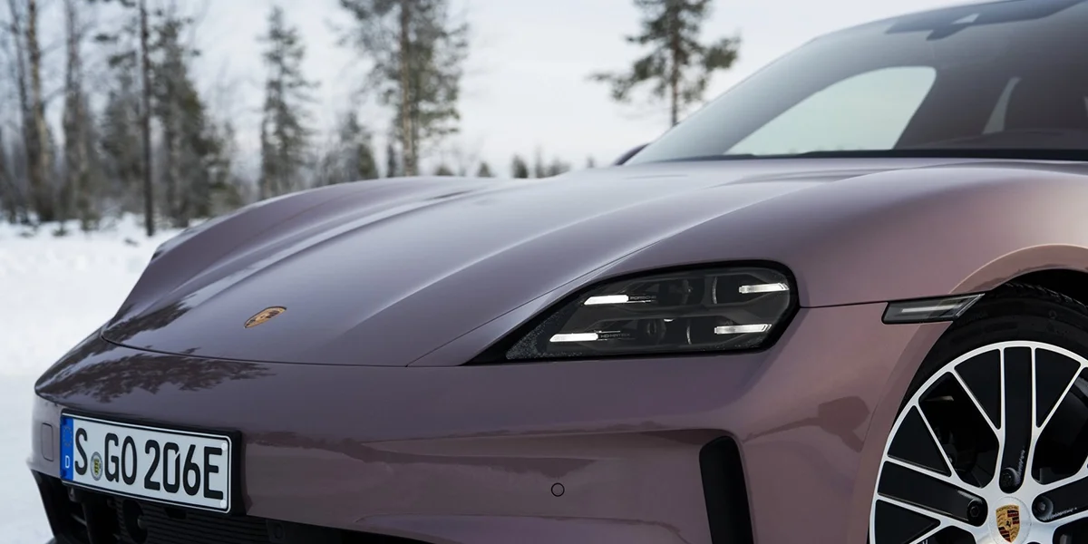 Front detail of Porsche Taycan showing headlights, hood, and wheel design against snowy forest backdrop.