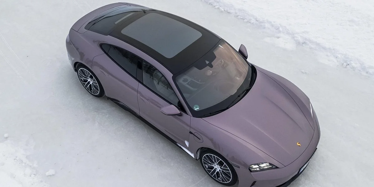Aerial view of Porsche Taycan driving down a snowy forest road, surrounded by winter trees.