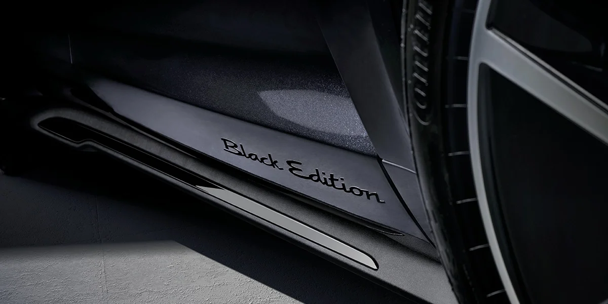 Aerial view of Porsche Taycan driving down a snowy forest road, surrounded by winter trees.