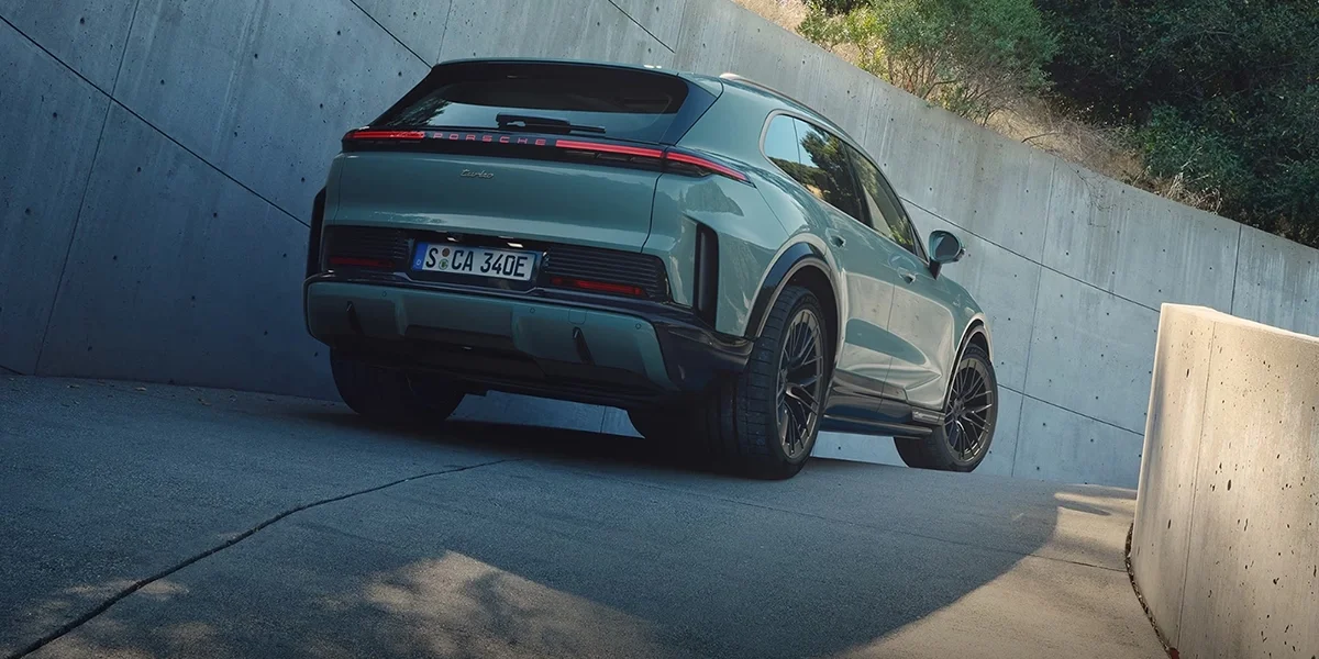 Porsche Cayenne seen from the rear on an inclined road, showing full-width taillight strip and turbo badge.
