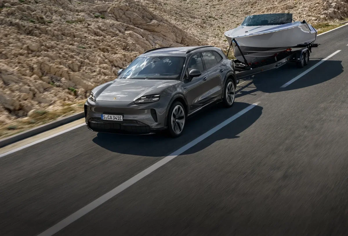 Gray 2027 Porsche Cayenne Electric towing a boat on a mountain road.