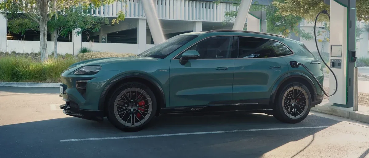 Green 2027 Porsche Cayenne Electric connected to an 800-volt fast-charging station.