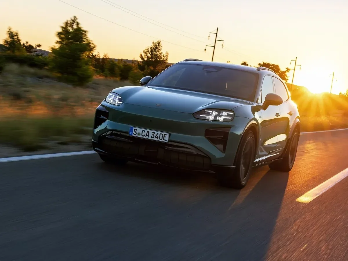 Green 2027 Porsche Cayenne Electric driving on a road at sunset.