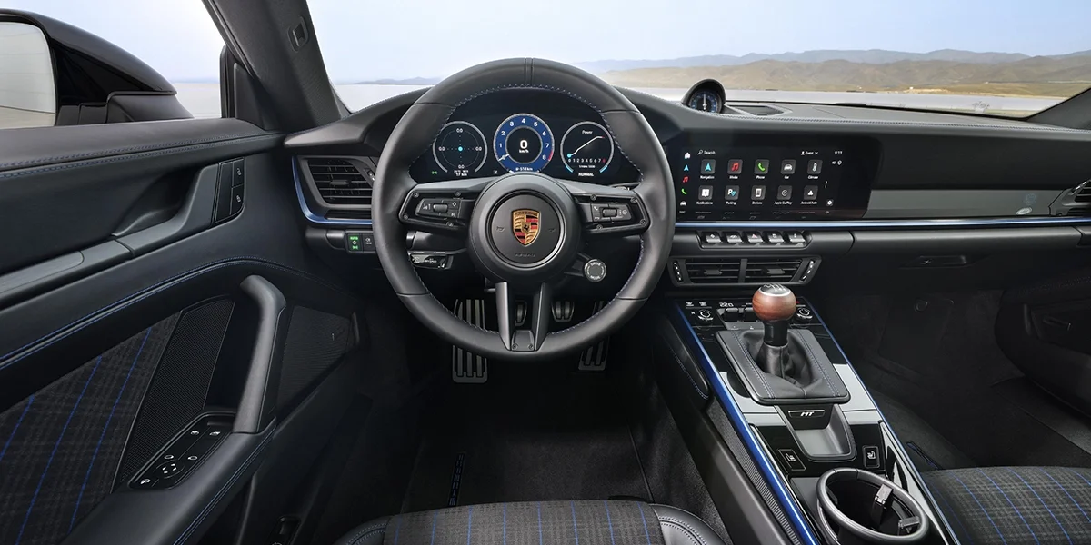 Cockpit view of 2026 Porsche 911 Carrera T showing digital gauge cluster and steering wheel.